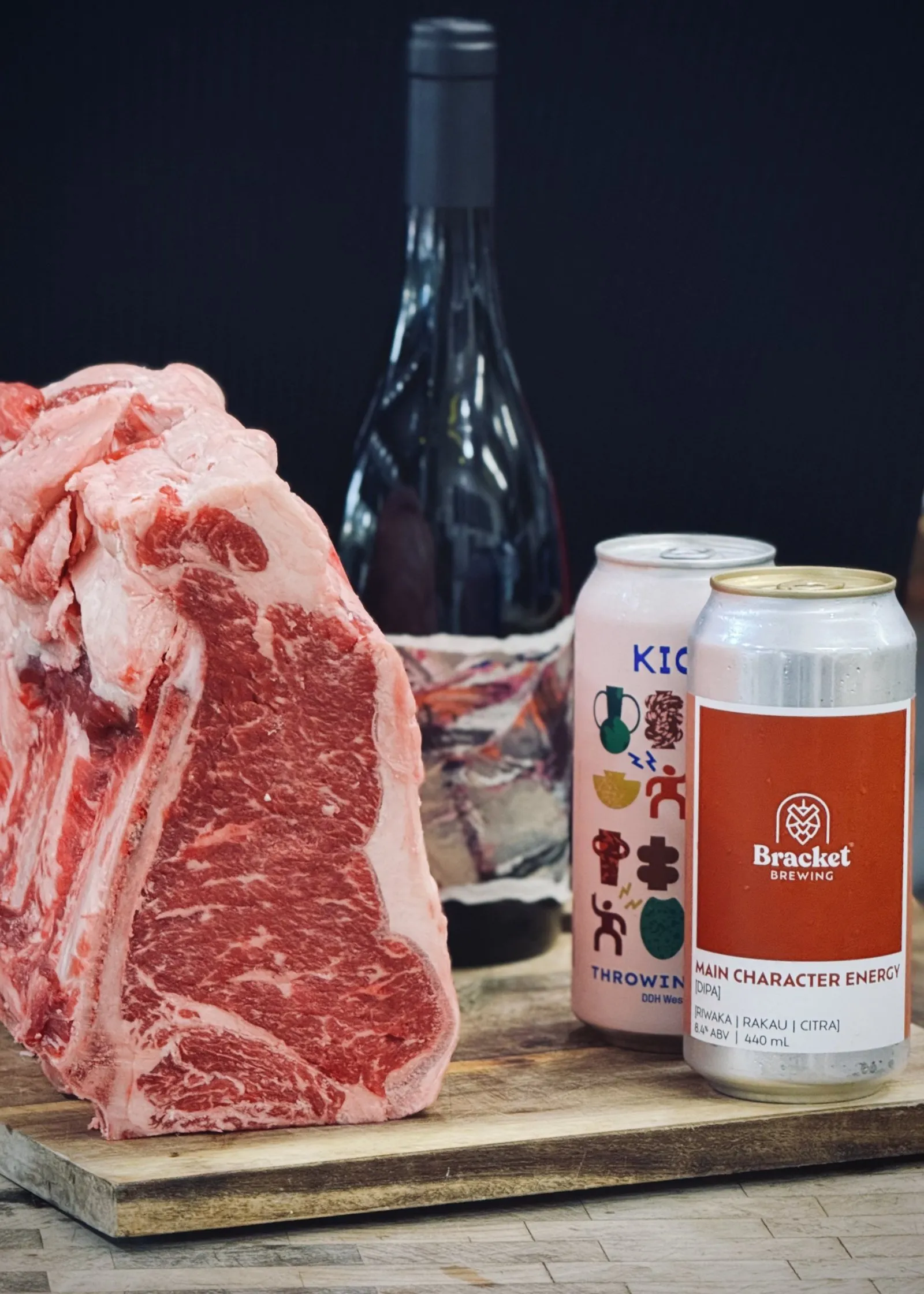 A rib of beef on a board with a bottle of wine and two cans of beer